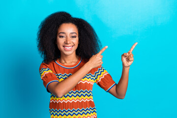Charming young woman in colorful t-shirt pointing with both hands on vibrant blue background