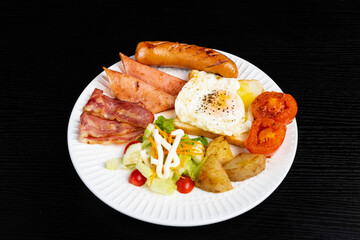 American breakfast set with eggs,bacon,toast, potatoes, tomatoes, mayonnaise sauce and sausage on black background.