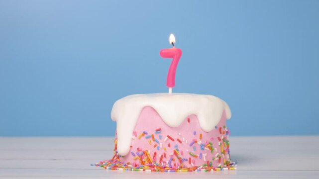 birthday cake with number seven candle to celebrate 7th birthday, seamless looping of cute cake with colorful candle number 7 for birthday annual celebrate party was lit, light blue background