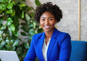 Fototapeta premium Confident Businesswoman in Stylish Blue Blazer with Curly Hair, Sitting at Desk with Laptop Surrounded by Indoor Plants in Modern Office Setting