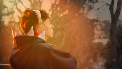 Young pensive boy listening to music with headphones at sunset