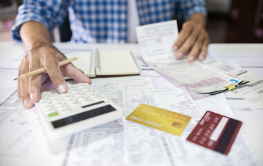 Asian man sitting at desk calculate receipt of expenses and all loan bills and try to find money to...