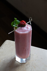 Fresh stawberry smoothie in a tall transparent glass, placed on marble top table, with classic cafe environment