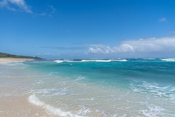 Pristine beach with turquoise waves and clear blue sky.
