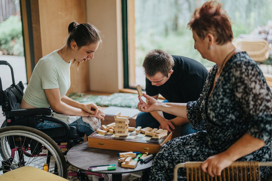 Heartwarming moment as a boy with Down syndrome, a girl in a wheelchair, and an elderly woman engage in a playful building blocks game, promoting inclusivity and inter generational bonding.