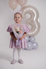 The image shows a young girl in a lavender dress embracing a sizable silver balloon in the shape of the number three.