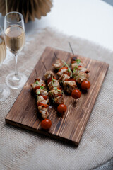 there is a wooden cutting board holding three skewers of grilled chicken and cherry tomatoes. 