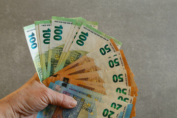 A close-up of a hand holding 20-euro 50-euro 100-euro banknotes against a gray surface.