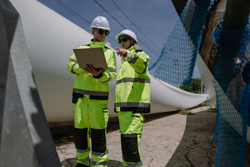 Fototapeta premium Maintenance engineer team standing at windmills at wind turbine farm. Skill people working outdoors at alternative renewable energy wind power station. Sustainable clean energy technology. Ecology