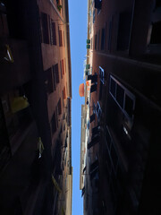 Narrow Alleyway with Tall Buildings and Blue Sky in Genoa, Italy