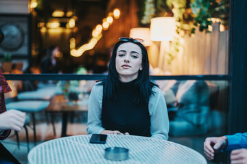 Young woman sitting confidently at an outdoor cafe table, engaged in a casual conversation with...