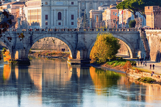 Close-up view of Ponte Sant'Angelo over the Tiber River in Rome, with autumn foliage, reflections in the water, and historic architecture. Rome, Italy - Powered by Adobe