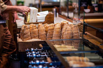 Hand of chef baker making Trdelnik, traditional tasty baked. Street food. Trdelnik bakery on the street market in Prague. Traditional Czech twisted buns rolled and grilled pastries.