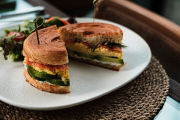 new york roll sandwich with croissant dough, smoked salmon, avocado, scrambled eggs or omelette styled with fresh greens, served in restaurant or cafe ready to eat
