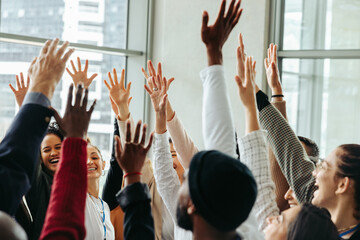 Engaged team with hands raised celebrating success in a modern office environment, showcasing...