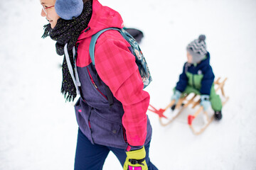 Mother dragging sled with child boy at snow and winter 