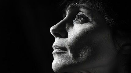 A woman's face is lit from the side, creating a dramatic black and white portrait.