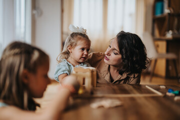 A loving mother engages with her young daughters, creating a warm family moment during indoor playtime. The image captures connection and affection in a cozy home setting.