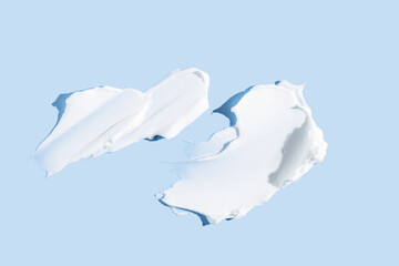 White cosmetic face cream or body lotion moisturizer strokes on pastel blue background. Hygiene, skincare product with creamy texture. Beauty face creme smear swatch on color background