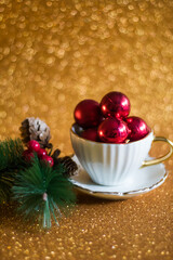 Simple Christmas concept: white tea cup filled with red Christmas tree baubles, spruce twig with mistletoe, golden blurry background
