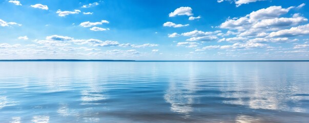 Fototapeta premium Scenic view of a serene lake mirroring puffy white clouds against a clear blue sky on a sunny summer day