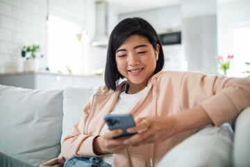 Smiling Asian woman using smartphone on couch at home