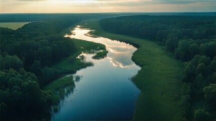 Obraz premium Serene river winding through dense green forests under a golden evening sky reflecting on the calm waters.