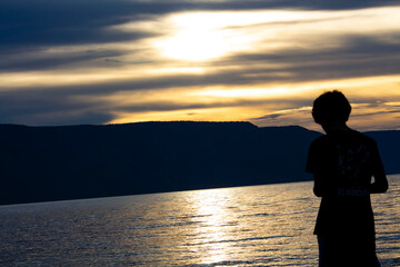 Fototapeta premium a person standing on the shore of a lake at sunset