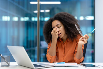 Young woman businesswoman appears stressed and tired at her desk in a modern office setting. She...