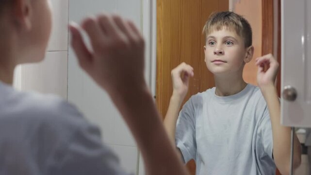 Teenage boy combs his hair in front of a bathroom mirror, focusing on styling his new haircut and enhancing his appearance during a morning grooming routine
