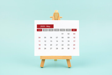 Calendar page for May 2025 with wood easel on a blue background.