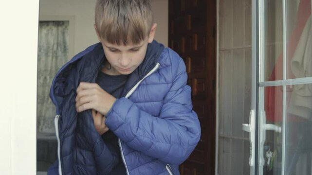 Young teenager zips up a blue winter jacket, getting ready to head outside. The scene captures a relaxed moment in a warm, inviting home setting