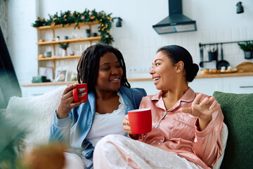 Two women share joyful moments while sipping coffee in a cozy living room adorned for the season.