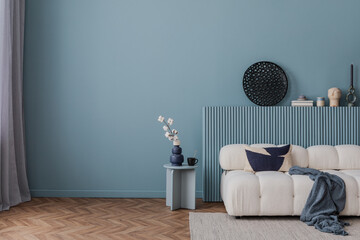 Modern living room in serene blue tones with a cozy white sofa, abstract decor, and a minimalist side table arrangement.