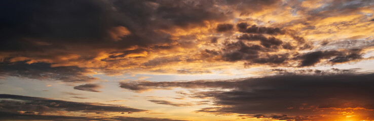 Obraz premium orange sunset in a cloudy sky with clouds at sunset in evening. Panoramic background with sky