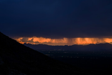 Vibrant sunset casting an orange glow over the mountains and illuminated clouds. A stunning contrast between the bright-lit horizon and dark silhouetted hills creates a breathtaking view.
