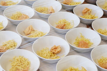 Several white bowls containing yellow noodles, fried foods and meatballs without sauce on the table