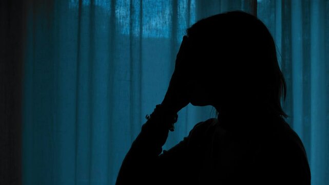 The silhouette of a girl stands alone at night, expressing despair and sorrow in the darkness.