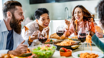 Happy multicultural friends having pasta dinner party at home - Multiracial people drinking red wine at lunch break - Food and beverage concept with diverse guys and girls dining together restaurant