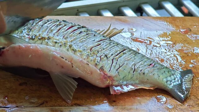 Hands cutting fish with knife.