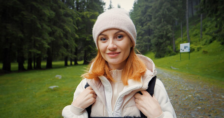 Red haired wanderer in a hat and hoody turns around and smile while walking through woods....