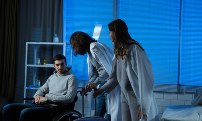 Obraz premium Adult man patient in hospital ready for discharge sitting in wheelchair and talking, friends supporting man helping with transportation.