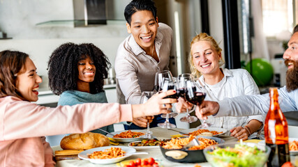 Diverse happy friends toasting red wine glasses at dinner party - Multiracial group of people having lunch break at bar restaurant - Life style concept with guys and girls eating mediterranean food
