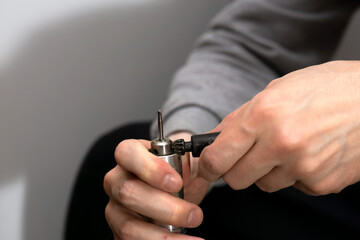 Replacing the nozzle on the burr grinder, men's hands with engraver close-up. 