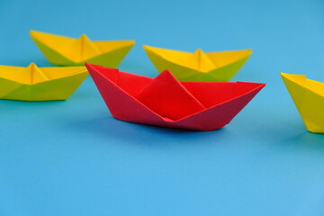 red paper ship or paper boats sailing ahead of other yellow paper ships on blue water.  flat lay with space for text. Uniqueness concept. success, leadership concept