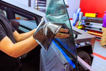 Worker technician applies window tint film to vehicle in workshop setting, focusing on precision...