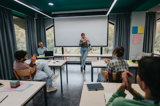 Female student stands confidently in front of classmates, delivering a project presentation in a modern classroom with attentive audience and discussion.
