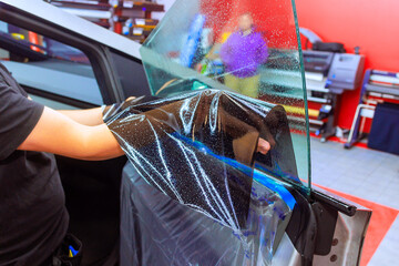 Technician worker applies window tint toa car door, ensuring an even finish while clients wait in...