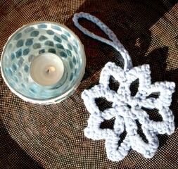 Hellblauer selbst gehäkelter Stern (handgefertigt) als Anhänger für Weihnachtsgeschenke oder Weihnachtsbaum, Windlicht mit blauem Mosaik, braune Porzellanteller. Nahaufnahme.