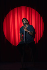 Happy young african american man comic tells stand up monologue on stage with red curtains. Concept...